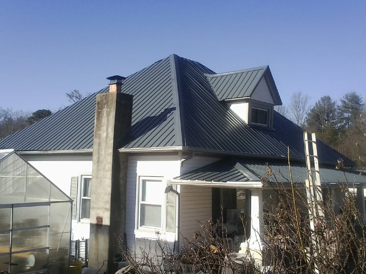Dark blue standing seam metal roof on a white farmhouse with dormer — Slate & Tile Roof Repair by Roofing Brothers in Mooreland